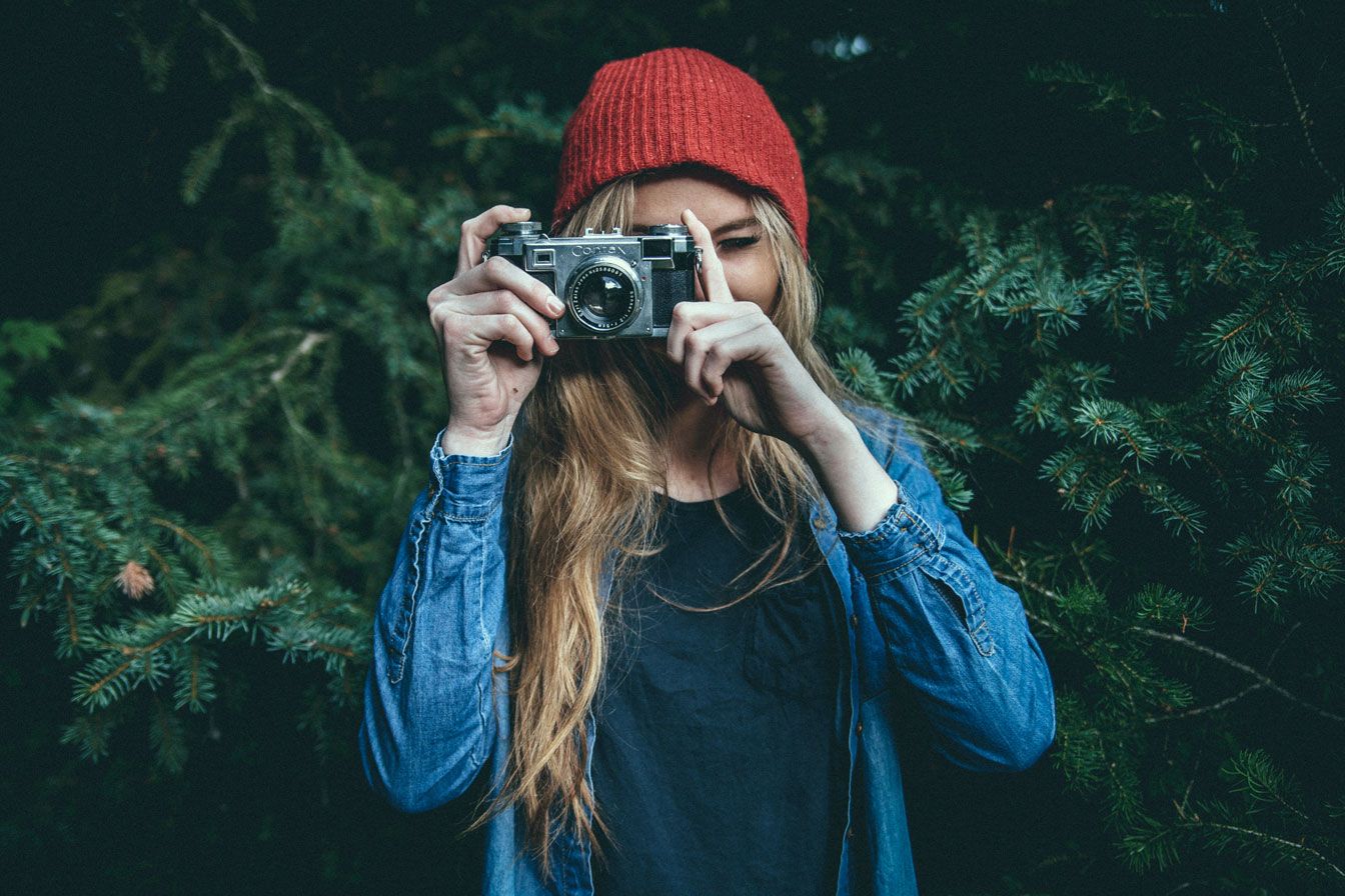 picture of a person with long, curly hair, wearing a red had taking a picture with an analogue camera